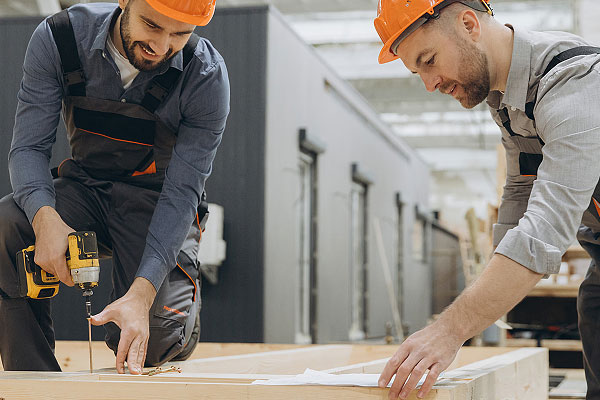 Two men in orange hard hats construct components of a single-family modular home