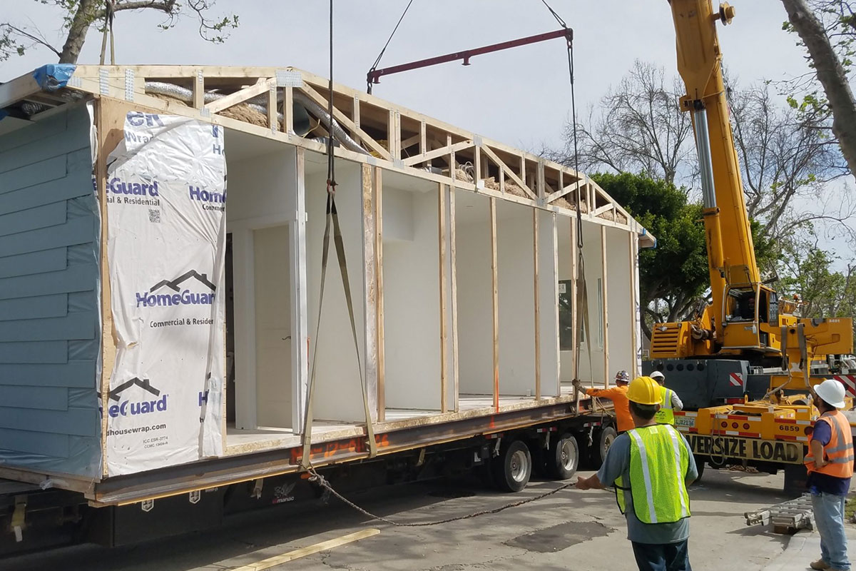 prefab-home-builder A prefab home being loaded onto a crane from a flatbed trailer in Los Angeles